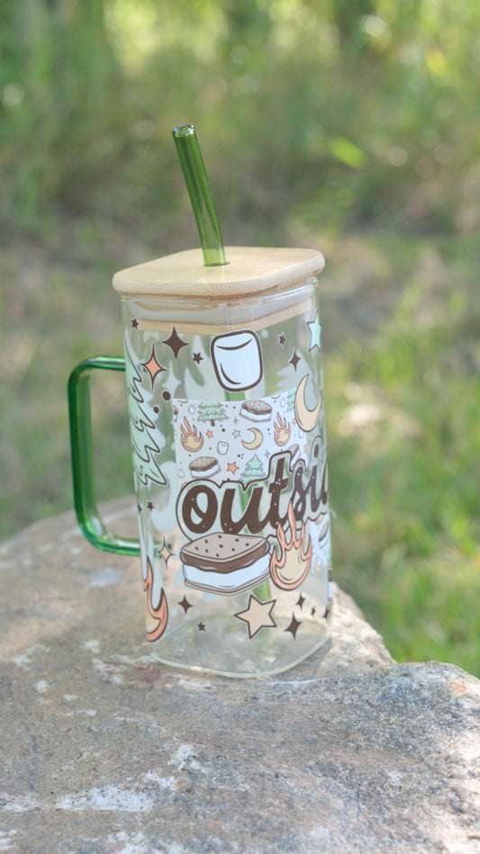 Square glass mug with wooden lid and green straw on a rock with a natural background